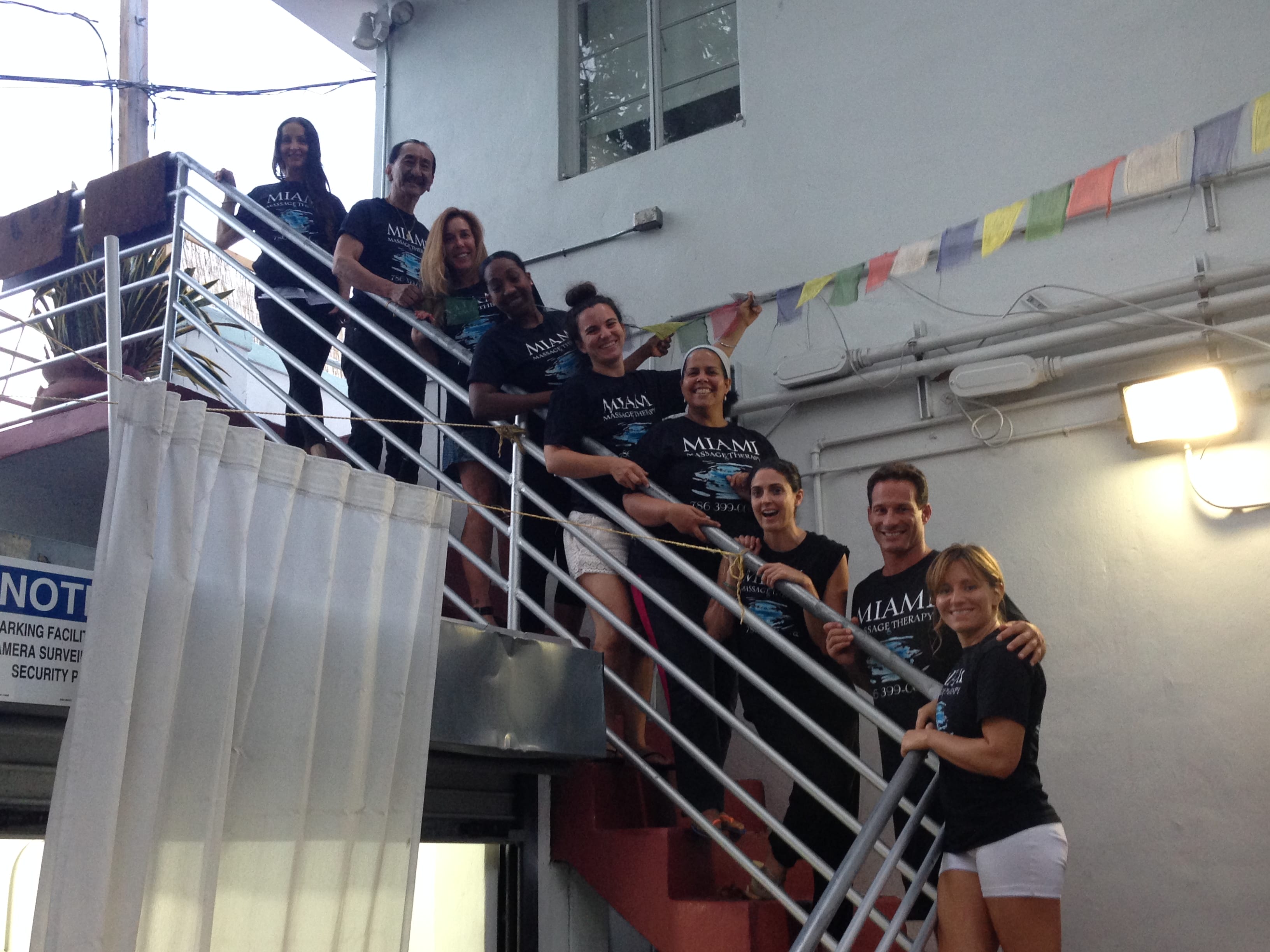 A group of people wearing matching shirts are standing on a staircase outside a building posing for a photo