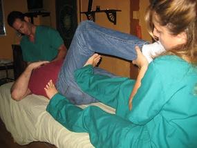 Two healthcare professionals assist a person lying on a table stretching their leg