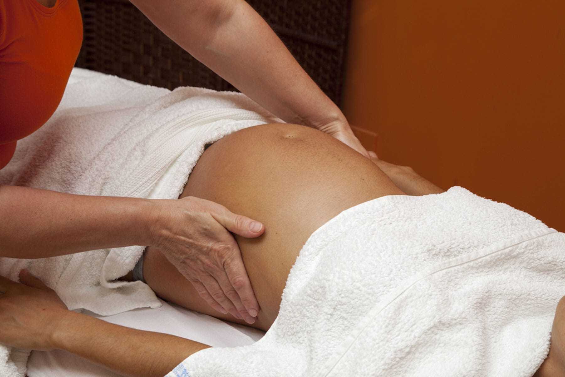 Person receiving a massage while covered with white towels a therapists hands are seen massaging their thigh