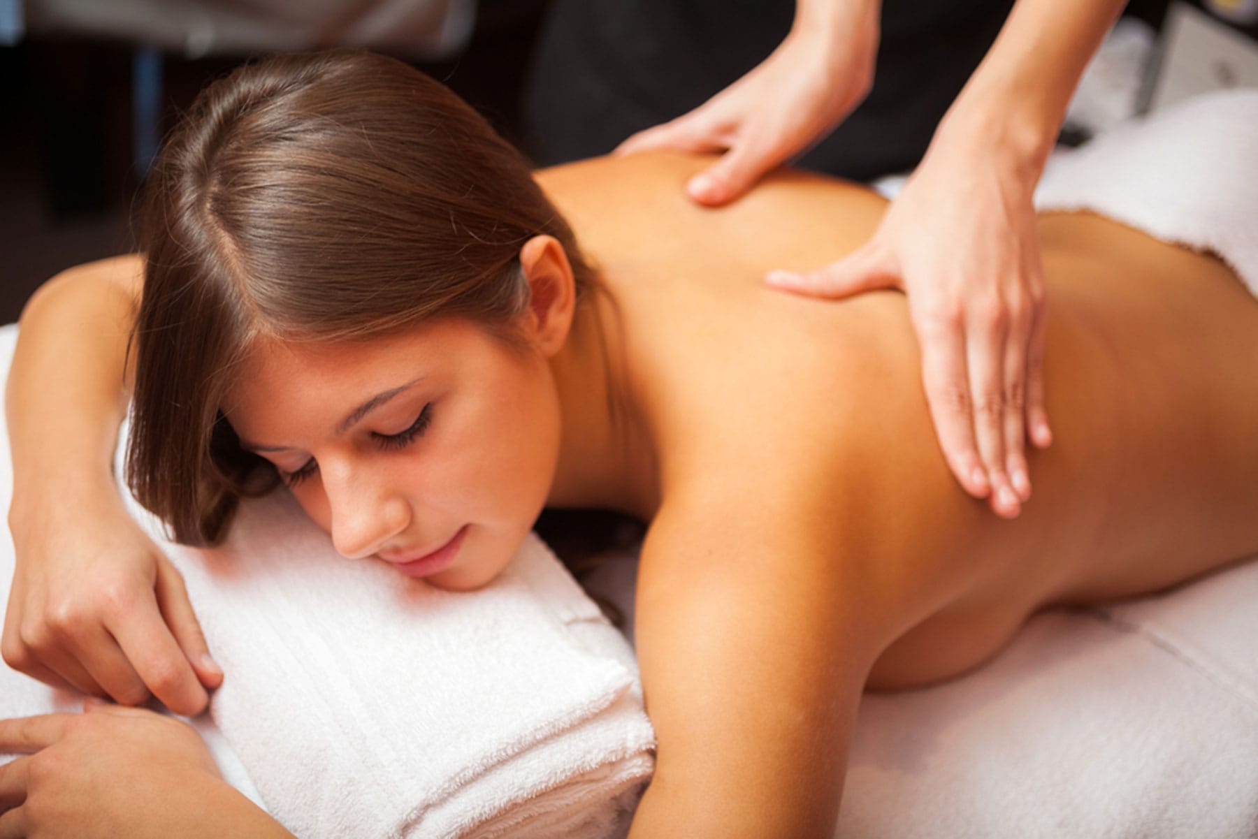 A person receiving a back massage while lying on a white towel with eyes closed