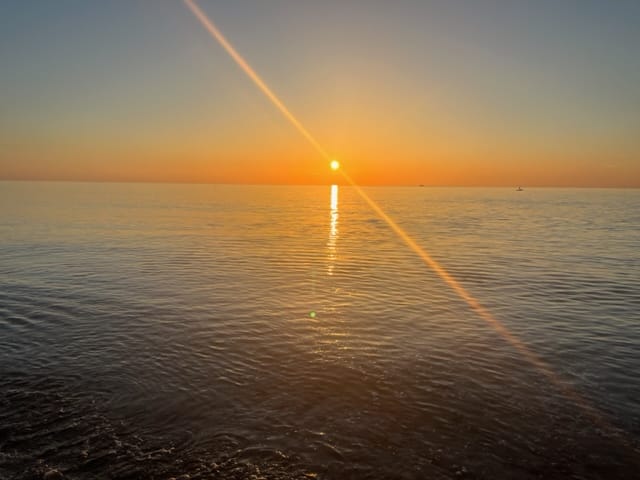 A serene sunset over a calm sea with the suns reflection creating a bright vertical line on the water