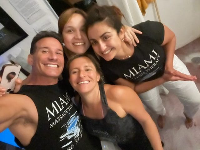 Four people smiling and posing together indoors The two people in front are wearing tank tops while the two people in the back are wearing t shirts that say MIAMI MASSAGE THERAPY