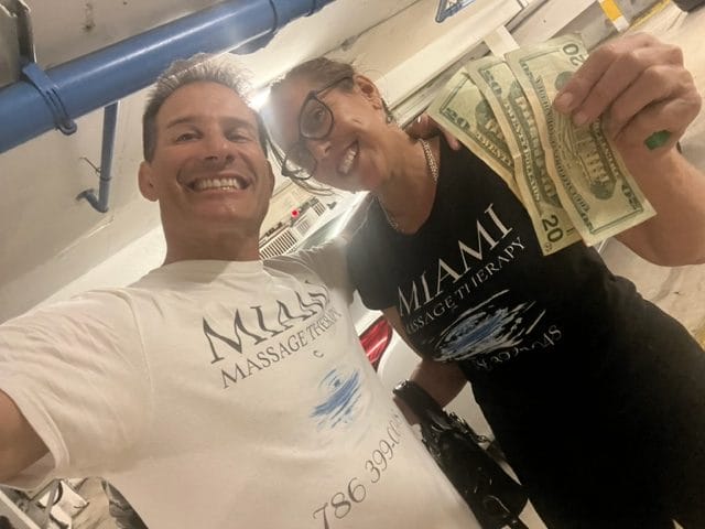 Two people smiling in a parking garage holding cash and wearing Miami Massage Therapy t shirts