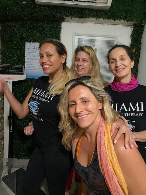 Four women smiling indoors with three of them wearing matching black Tshirts that read MIAMI LIFE THERAPY | Miami Massage Therapy best female massage therapists