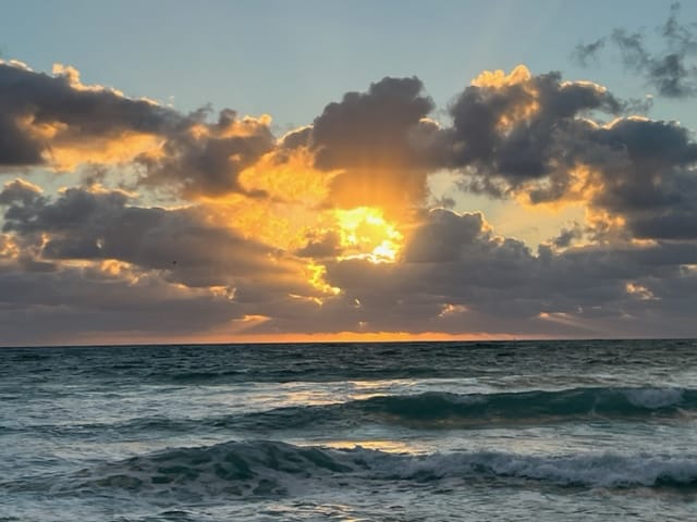A sunset over a wavy ocean with the sun partially obscured by clouds that are illuminated with golden light