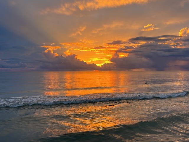 A vibrant sunset over a calm ocean with orange yellow and blue hues reflected in the water and waves gently rolling in